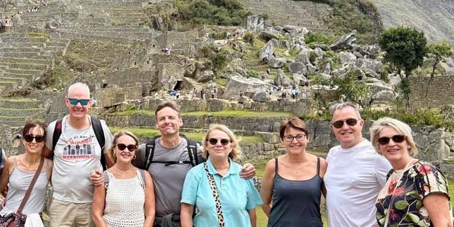 Group of seven people posing at Machu Picchu in Peru, with ancient stone terraces and ruins behind them. 